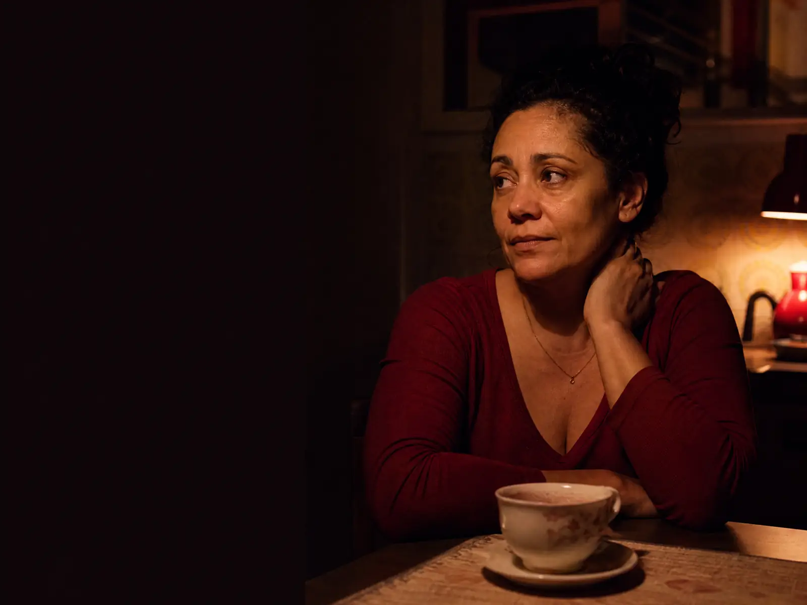 Mulher sentada sozinha à mesa da cozinha à noite, pensativa